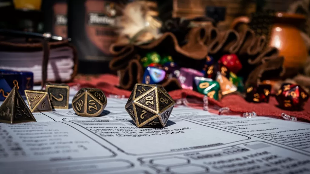 Low angle image of a brass 20-sided die on a character sheet in the sun. In the background are a dice bag and a notebook. - Esther Derkson